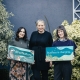 three women stand in a leafy garden, 2 holding signs with nature illustrations and slogans 'Business is changing...'and #ForNature
