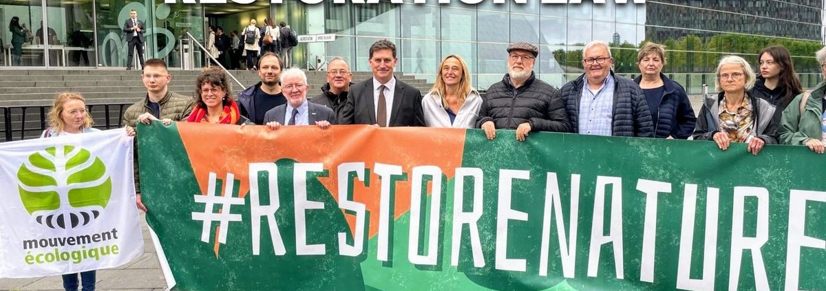 Group of people hold banner in shades of orange and green with white text #RestoreNature