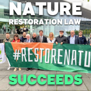 Group of people hold banner in shades of orange and green with white text #RestoreNature