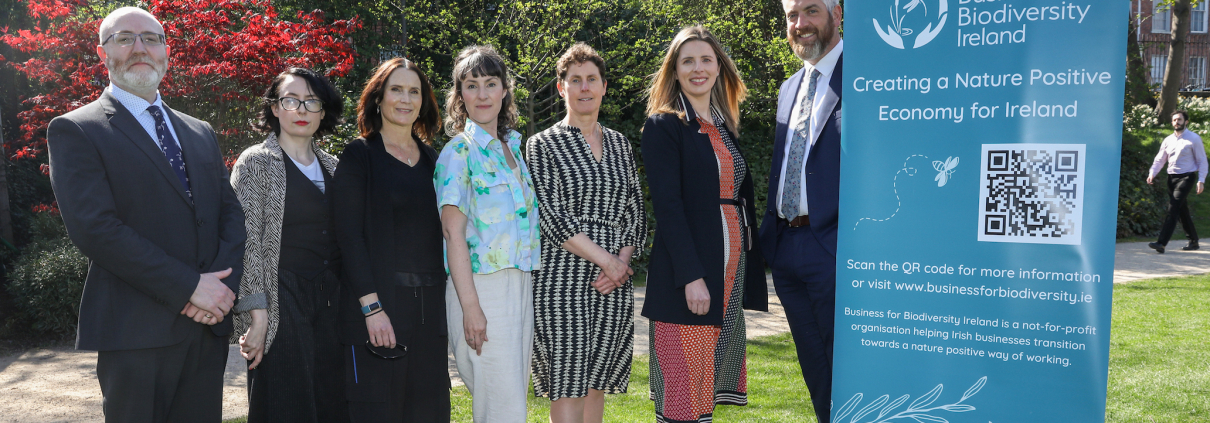 People in a park on a sunny day standing next to a teal pull-up poster with logo