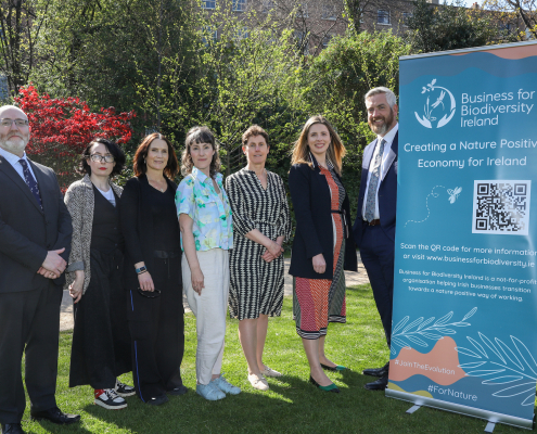 People in a park on a sunny day standing next to a teal pull-up poster with logo