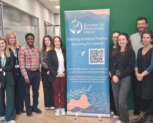 Group of people in an office with green walls beside a pullup posted with a QR code