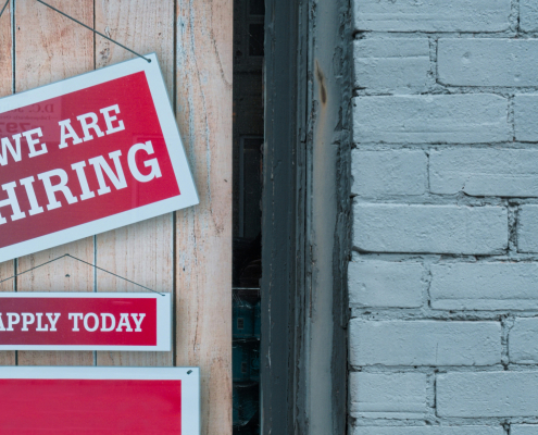 Picture of a door with a red sign with white text reading 'We are hiring'