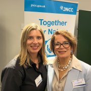 Two women at an event a poster in white a blue behind them reads Together for Nature