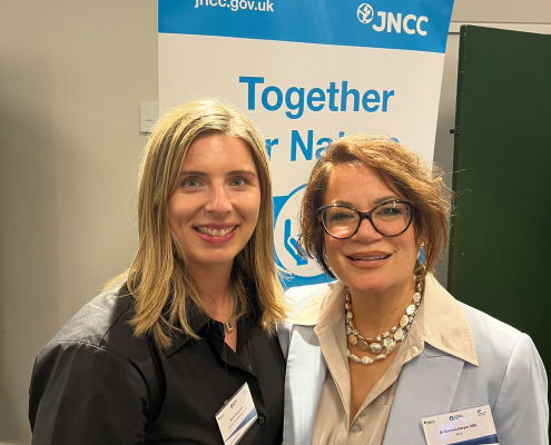 Two women at an event a poster in white a blue behind them reads Together for Nature