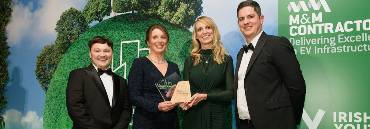 Two women and two men in evening wear, holding an award against a backdrop with illustrations of trees
