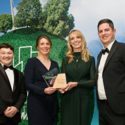 Two women and two men in evening wear, holding an award against a backdrop with illustrations of trees