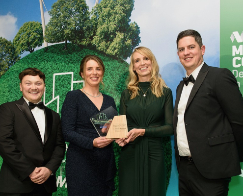 Two women and two men in evening wear, holding an award against a backdrop with illustrations of trees